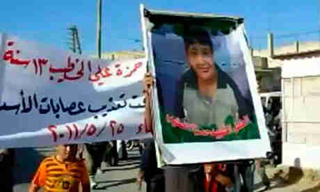 Protester holding up a picture of Hamza al-Khatib during his funeral (Guardian/AFP)