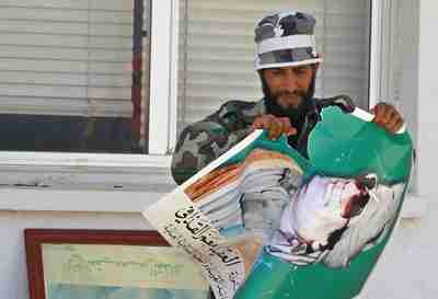 A rebel fighter destroys a Gaddafi poster (Reuters)