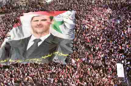 Pro-Syrian regime protesters carry a huge portrait of President Bashar Al Assad during a demonstration to show their solidarity in Damascus (AP)