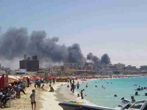 Egyptians enjoy the beach while fires and riots burn in the background