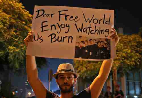 Syrian man in front of United Nations building in Beirut holds up placard saying, 'Dear Free World, Enjoy watching us burn.' (AP)