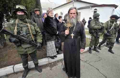 An Orthodox priest holds a crucifix next to armed men in military fatigues blocking access to a Ukrainian border guards base in Crimea on Sunday (AFP)