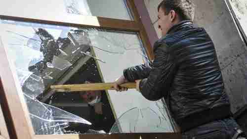 Pro-Russian protester breaks a window of a government building in Donetsk on Sunday (BBC)