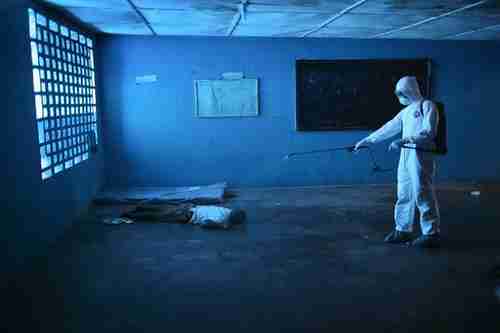 A health worker disinfects a corpse in an Ebola isolation ward, once a primary school, in Monrovia (National Geographic)