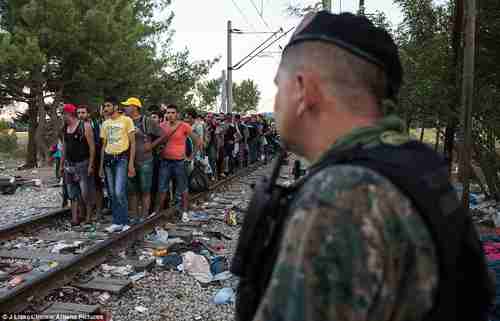 Hundreds of migrants stand in line on a railway track as uniformed police watch on (Athena Pictures)