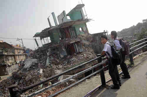 Nepalese students wait for school bus in front of a collapsed house (AP)