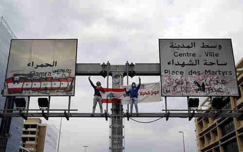 Anti-government protesters in Beirut, Lebanon, stand atop a road sign and flash the victory sign along a main highway that has been blocked by hundreds of protesters, on Friday. (AP)