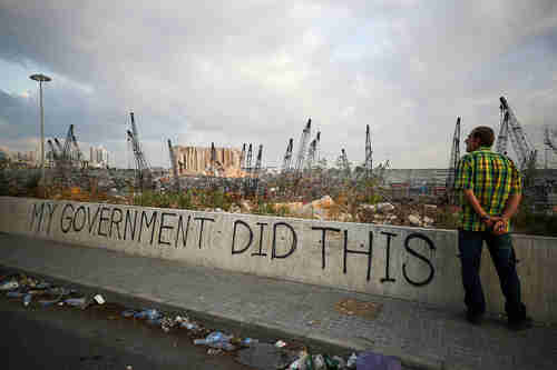 A man stands near the Beirut blast site on August 11.  Graffiti reads 'My government did this' (Reuters)